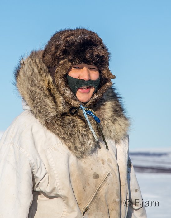 A young woman dressed approperately for riding behind a snow-go on a sled. 