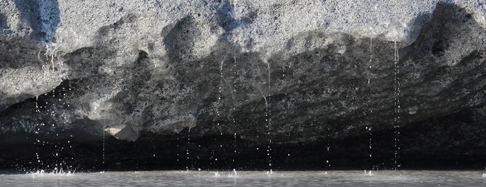 A sun-drenched ice face releases tiny cascades of muddy water.