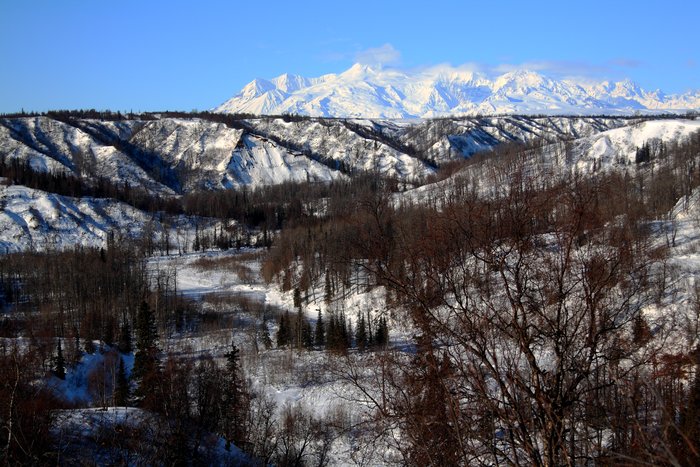 The frozen Chuitna River winds between sedimentary bluffs near the proposed site of the Chuitna Coal Mine, while volcanic Mt. Spurr towers in the distance.