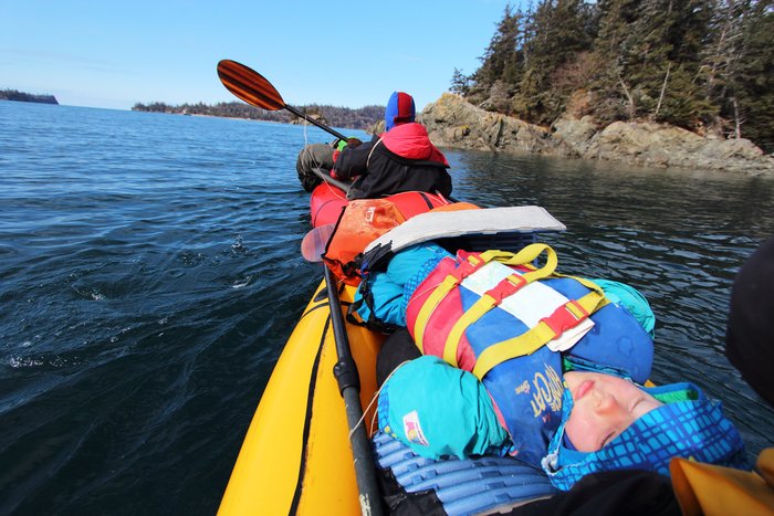 Katmai naps in a packraft "long boat" - two boats tied together atop a wood pole.