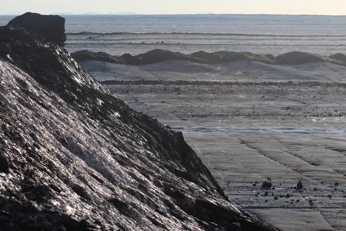 A vast plain of smooth ice stretches out from long hills of rocky ice.