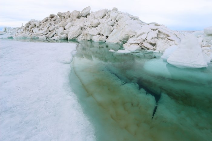 Dark blue water in the bottom of a pool around a thawing ice pile