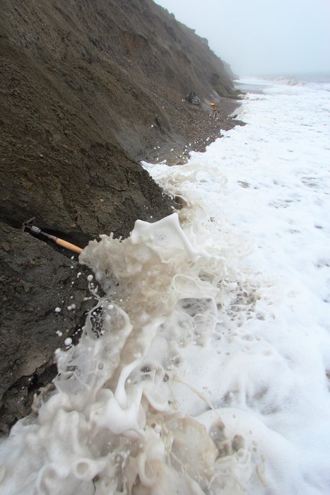 A warm August day, and waves wash against the permafrost and sandy mud of Barter Island.