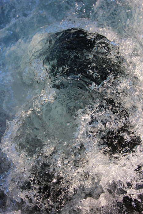 Looking into a shadowy hole in the ice, through roiling water.