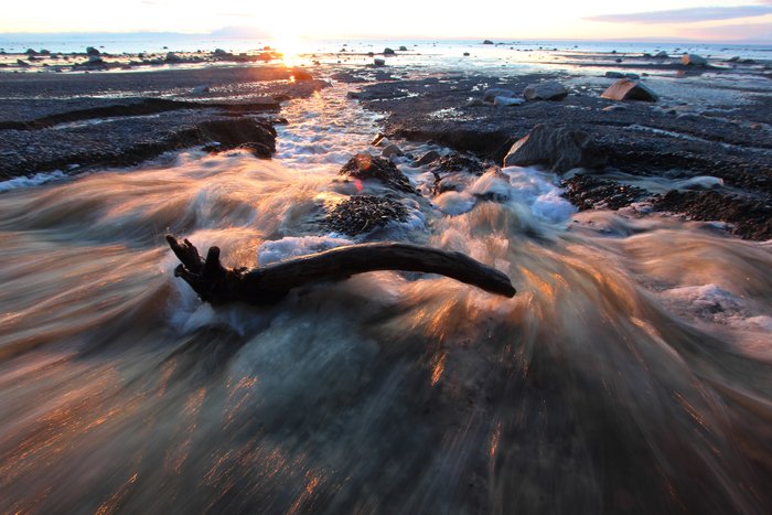 A stream swoolen by spring melt flows over winter's ice at sunset.