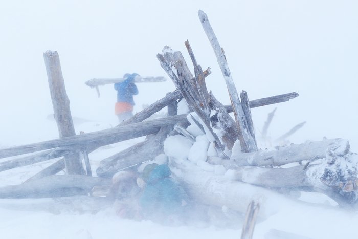 Hig carries logs to help barricade our tent site against the wind.  Lituya and Katmai hunker behind the partially completed wall.